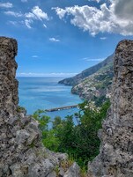 Vista costera con acantilados rocosos, un muelle con barcos y un pueblo en una ladera.