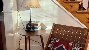 Een houten stoel met een gestreept kussen, een klein rond tafeltje met een lamp, en een trap met houten leuningen.