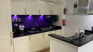 Una cocina moderna con armarios blancos, encimera negra y una salpicadera iluminada con luz púrpura.