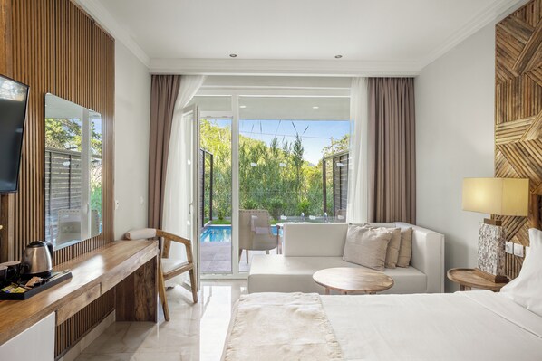 Ein modernes Hotelzimmer mit einem Holztisch, einem Bett, einer Couch und Blick auf einen Swimmingpool und Grünflächen.