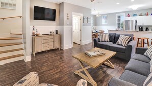 A spacious living room with a wooden coffee table, a gray sofa with striped cushions, and a TV mounted on the wall. - SEAS THE DAY IS A PRIVATE 2BD COTTAGE WITH 3 COMMUNITY POOLS, PET FRIENDLY! (Port St Joe)