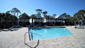 A pool area with a clear blue pool, lounge chairs, and a brick walkway. - SEAS THE DAY IS A PRIVATE 2BD COTTAGE WITH 3 COMMUNITY POOLS, PET FRIENDLY! (Port St Joe)