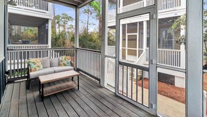 A covered porch with a sofa and bench, large windows, and a view of the surrounding area. - SEAS THE DAY IS A PRIVATE 2BD COTTAGE WITH 3 COMMUNITY POOLS, PET FRIENDLY! (Port St Joe)