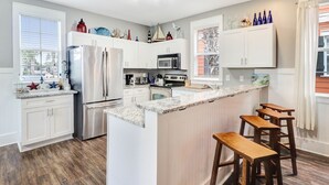 A modern kitchen with white cabinetry, a stainless steel refrigerator, a microwave, and a wooden island with bar stools. - SEAS THE DAY IS A PRIVATE 2BD COTTAGE WITH 3 COMMUNITY POOLS, PET FRIENDLY! (Port St Joe)