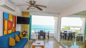 Una camera d'albergo con un divano blu, un tavolino, una ventola a soffitto e vista sull'oceano.