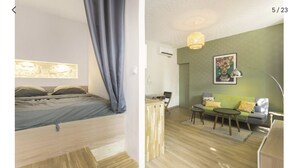 Une chambre avec un lit, une table de chevet et une fenêtre avec des rideaux. La pièce est dotée d’un plancher en bois et d’un mur de couleur claire.