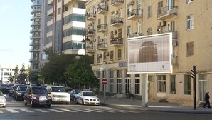 Una veduta di una strada con edifici a più piani, un attraversamento pedonale e auto parcheggiate.