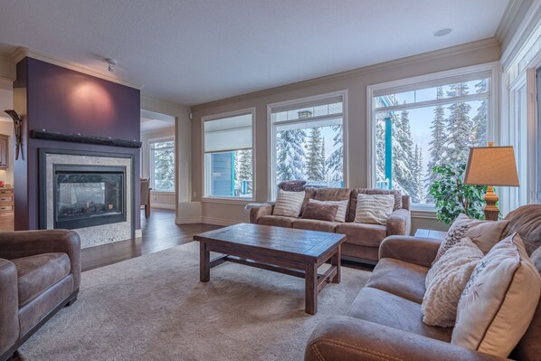 Relax by the fireplace in this inviting living room with a view of snow-covered trees.