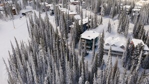 Luchtbeeld van een met sneeuw bedekt wintersportresort met meerdere gebouwen, omringd door dichte altijdgroene bomen.