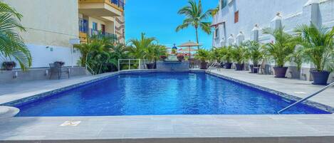 A swimming pool with a tiled deck, surrounded by potted plants and outdoor furniture.