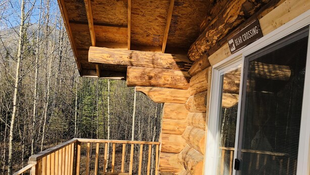 A wooden cabin with a deck, a bench, and a chair. - Wrangell Mountain Lodge (Chitina)