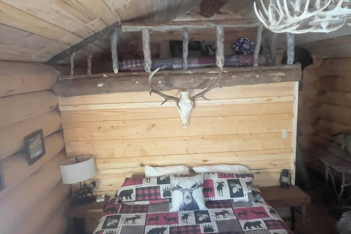 Un dormitorio tipo cabaña de madera con cabecera de madera, cráneo de venado y cuernos sobre la cama.