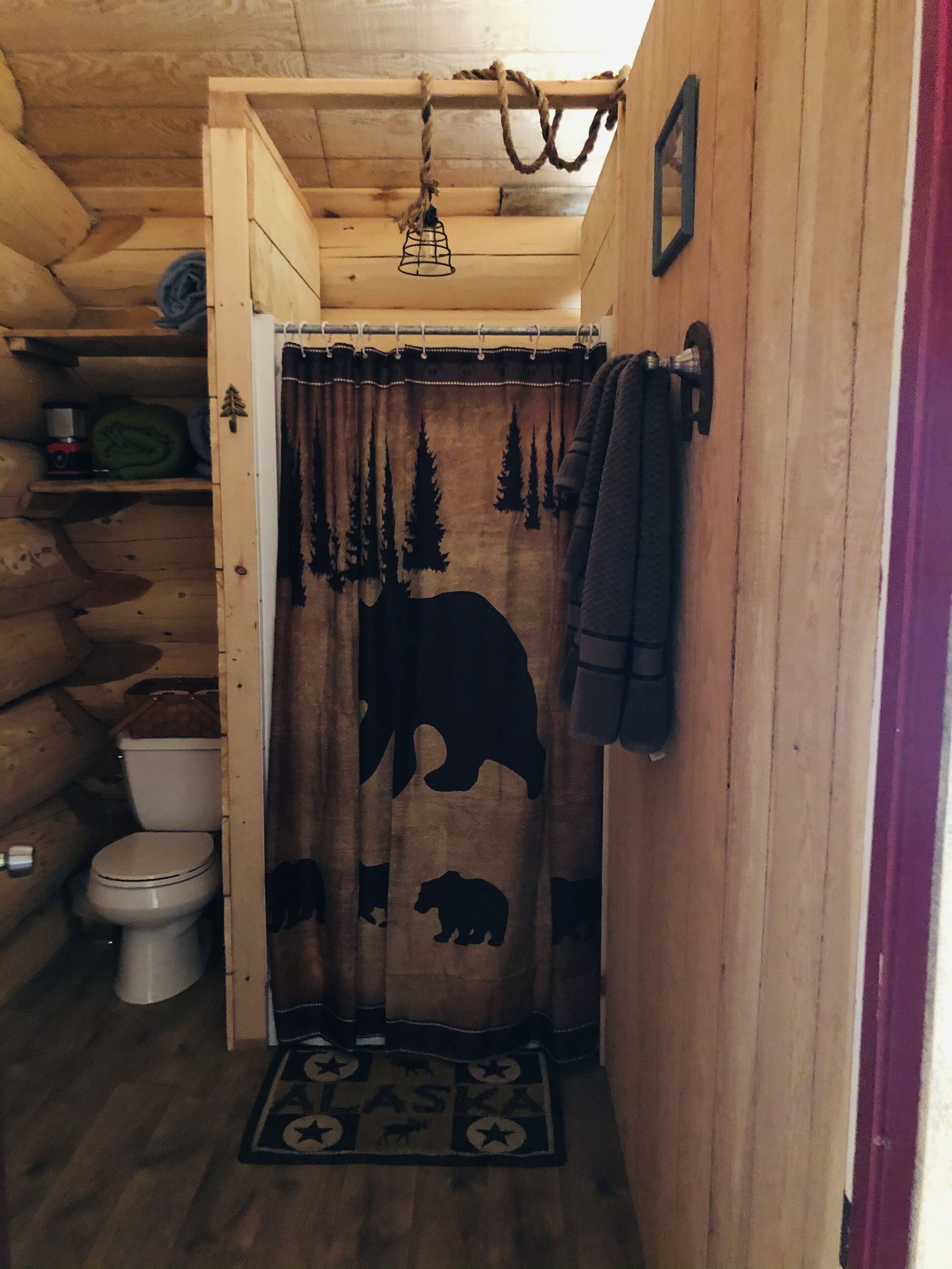 Baño de cabaña de madera con cortina de ducha temática de oso, un inodoro y una alfombra pequeña con diseño de oso.