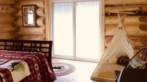 A log cabin room with a bed, a fireplace, a window, and a teepee. - Wrangell Mountain Lodge (Chitina)