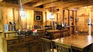 A rustic wooden kitchen with a wooden table and chairs, a coffee maker, and various kitchen utensils. - Wrangell Mountain Lodge (Chitina)
