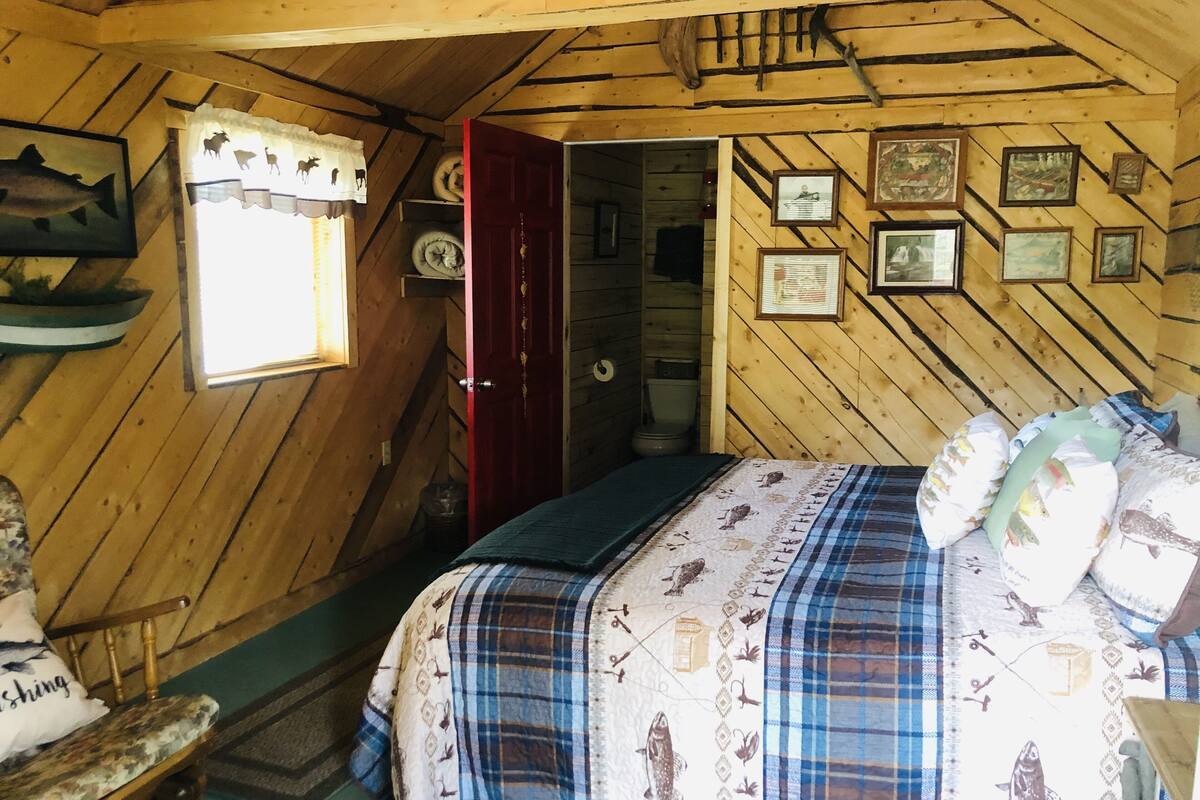 Un dormitorio de cabaña acogedor, con cama, una silla y una ventana con cortinas.