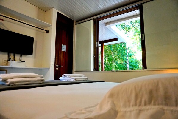 Una habitación de hotel con una cama, un televisor de pantalla plana montado en la pared, una ventana con vistas a zonas verdes y una puerta.