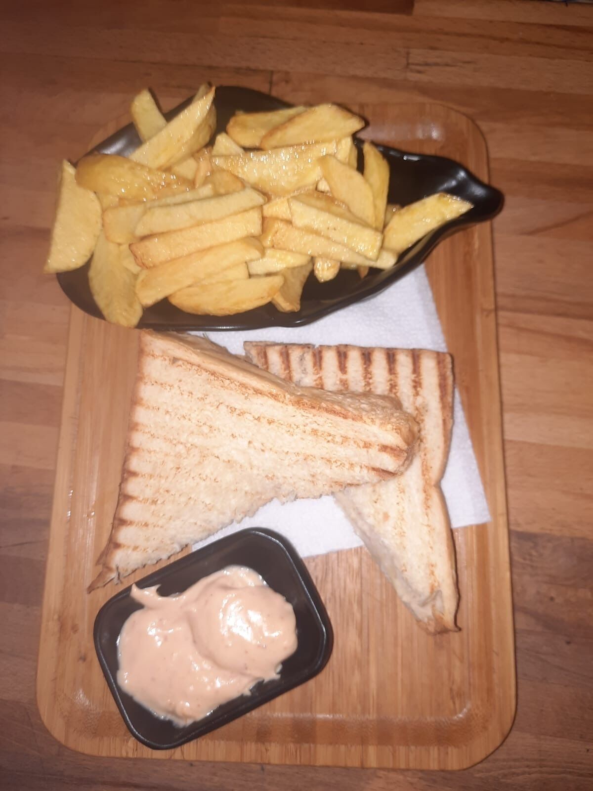 Una bandeja con un sándwich de queso a la plancha, papas fritas y un recipiente pequeño de salsa.