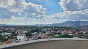 A panoramic view of a town with a prominent white building in the foreground, a wide road, and distant mountains under a partly cloudy sky. - Rezidenca Shopi Apartments (Elbasan)