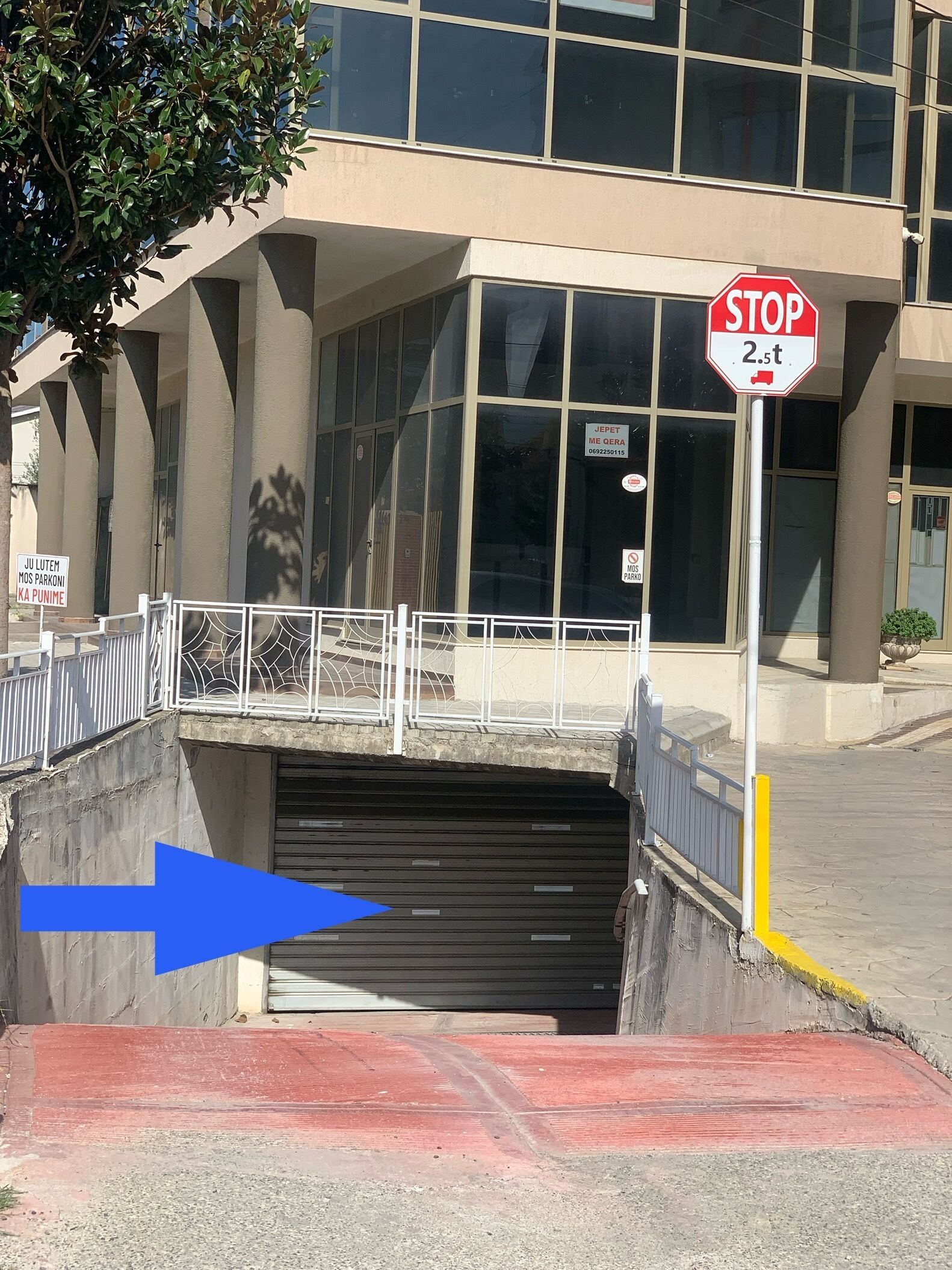 A building with a stop sign, a metal gate, and a blue arrow pointing towards a garage entrance.
