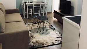 A living room with a sofa, a dining table with chairs, a TV, and a refrigerator. - Rezidenca Shopi Apartments (Elbasan)