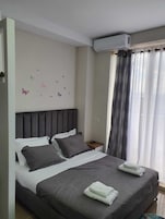 A modern hotel room with a large bed, grey bedding, a headboard, a bedside table, a remote control, and a window with curtains.
