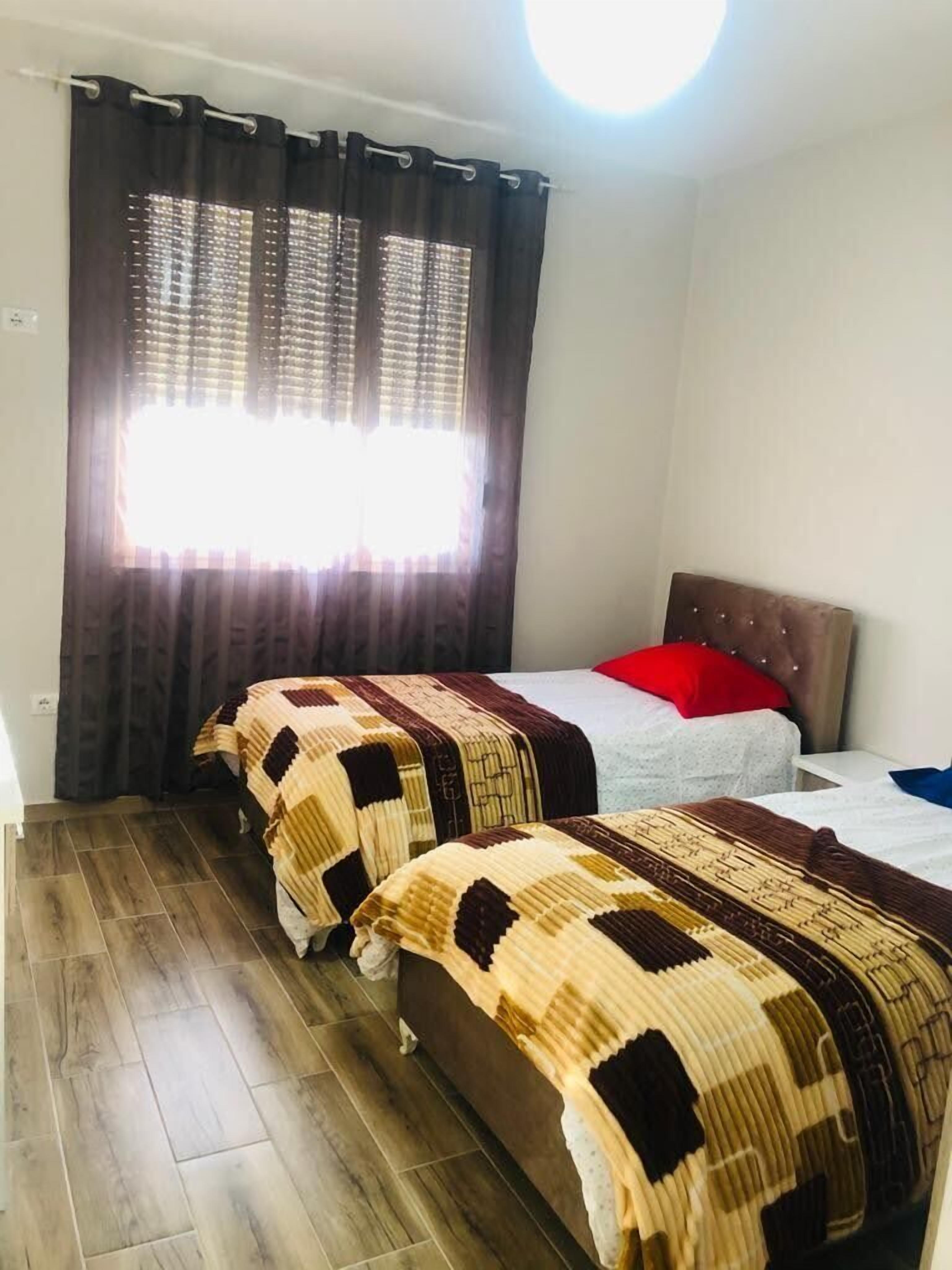 A bedroom with two beds, a window with curtains, a headboard, and a wooden floor.