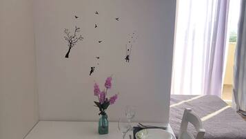 A dining area with a white table, two chairs, a vase with flowers, and wall decals of birds and a tree.
