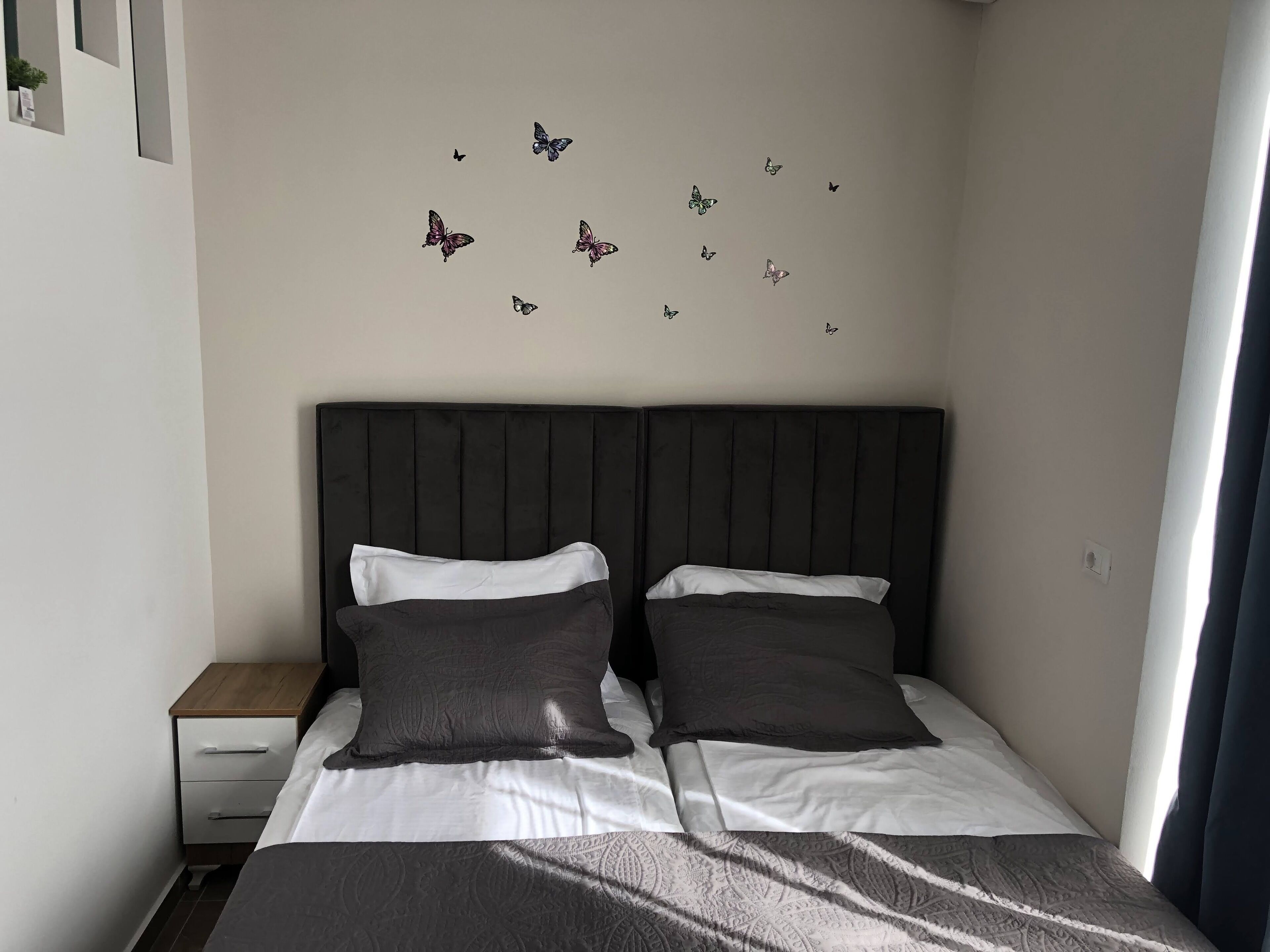 A bedroom with a bed, two pillows, a nightstand, and butterfly decals on the wall.