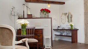A bathroom with a wooden vanity, a white chair, and a vase with white flowers.