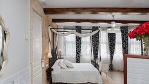 A bedroom with a four-poster bed, a chandelier, and a vase with red flowers.