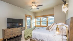 A bedroom with a bed, a TV, a wooden dresser, and a ceiling fan. - 3BR Big Sky Townhome | Walk to Town Center, Hot Tub & Sleeps 12 (Big Sky)