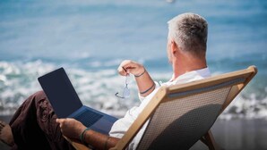 Eine Person benutzt einen Laptop auf einem Liegestuhl mit Blick auf das Meer.