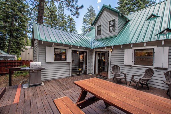 A wooden deck with a grill, picnic table, and Adirondack chairs.