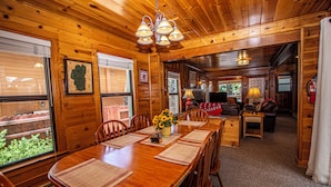 A wooden interior with a dining table set for four, a chandelier, and a view through a window. - Fir Forest Cottage by Hauserman Rental Group (Tahoe City)