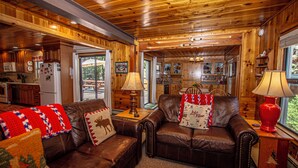 A cozy cabin interior with wooden walls, a brown leather sofa, and a kitchen area. - Fir Forest Cottage by Hauserman Rental Group (Tahoe City)