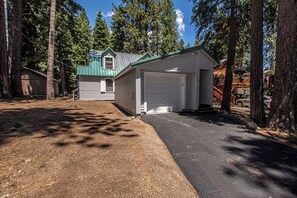 Une maison à deux étages avec un garage, entourée de grands arbres et sous un ciel dégagé.