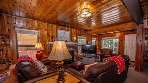 A wooden interior with a fireplace, leather sofa, and a television. - Fir Forest Cottage by Hauserman Rental Group (Tahoe City)