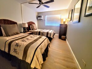 Une chambre d’hôtel avec deux lits, un ventilateur de plafond, un appareil de climatisation, une fenêtre avec des stores et une lampe de chevet.