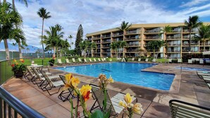 Ein Hotelpoolbereich mit Liegestühlen, einem großen Pool und einem mehrstöckigen Gebäude mit Balkonen.