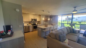 Eine moderne Küche mit Edelstahlgeräten, ein Essbereich mit Bar und ein Wohnzimmer mit Sofa und Blick ins Freie.
