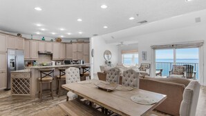 A spacious kitchen with modern appliances, a dining area with a wooden table and cushioned chairs, and a balcony with a view of the ocean. - Condos directly on the Gulf (Destin)