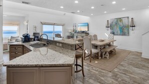 A spacious kitchen with a large island, a dining area with a view, and a living area with a TV and artwork. - Condos directly on the Gulf (Destin)