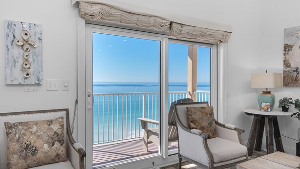 A room with a view of the sea, a white sofa, a chair, a small table with a lamp, and a painting on the wall. - Condos directly on the Gulf (Destin)