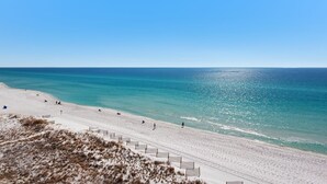 A beach with a clear sky, sandy shore, and a few people walking. - Condos directly on the Gulf (Destin)