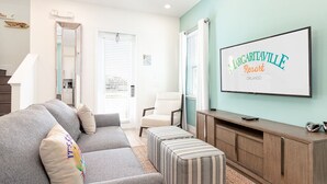 Een woonkamer met een grijze bank, gestreepte poefs, een houten tv-meubel en een lijst met de tekst LARGARTAVILLE Resort in Orlando.