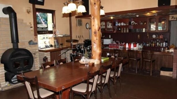Un comedor con una larga mesa de madera y sillas, una barra con estantes llenos de botellas y un estufa de leña.