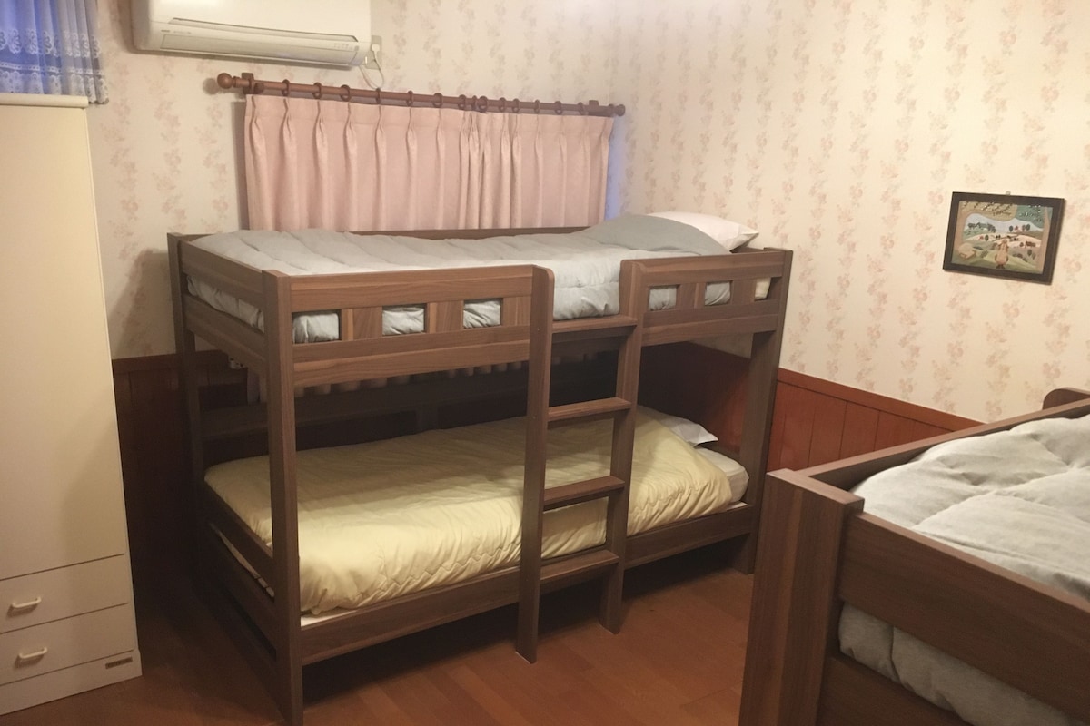 A bunk bed room with a wooden headboard, a small bedside table, and a wall-mounted air conditioner.
