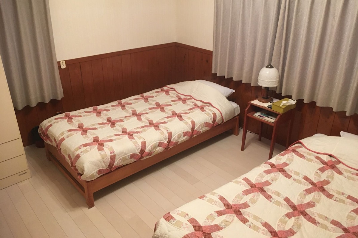 A room with two single beds, a bedside table with a lamp, and a small table with a box.