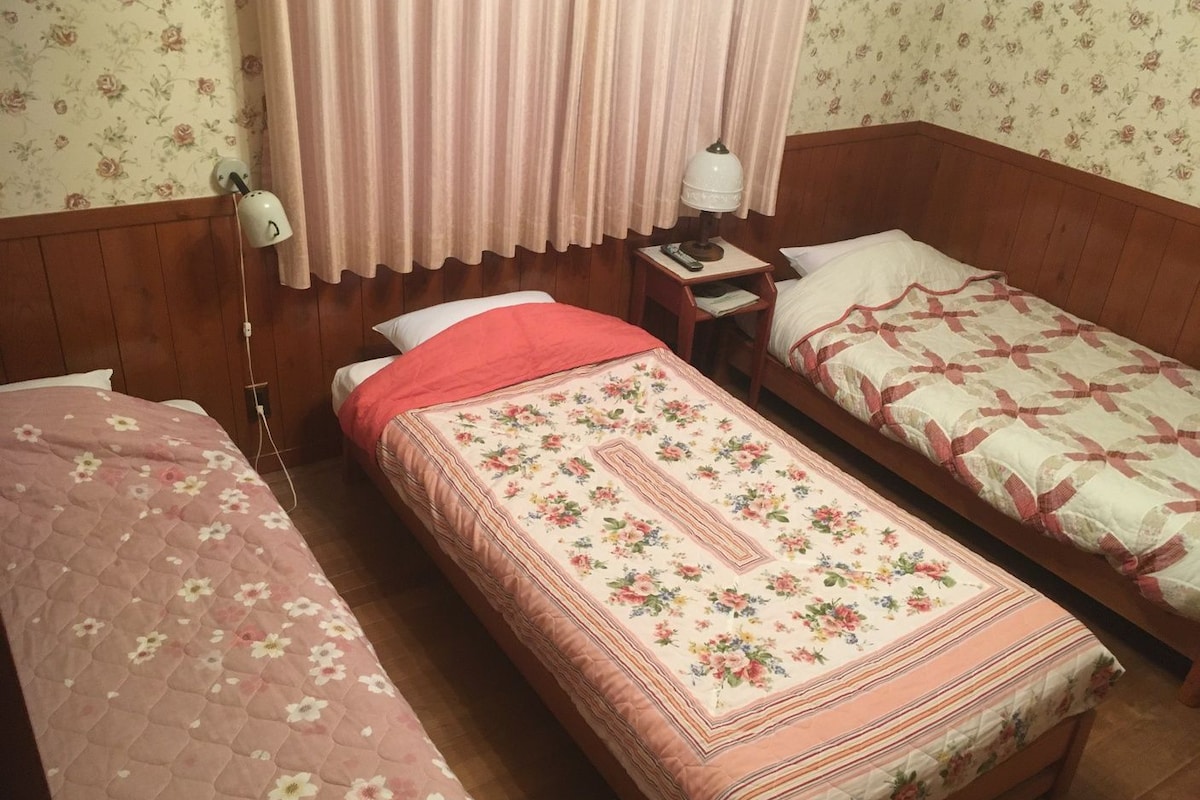 A room with two single beds, a nightstand with a lamp, and floral wallpaper.